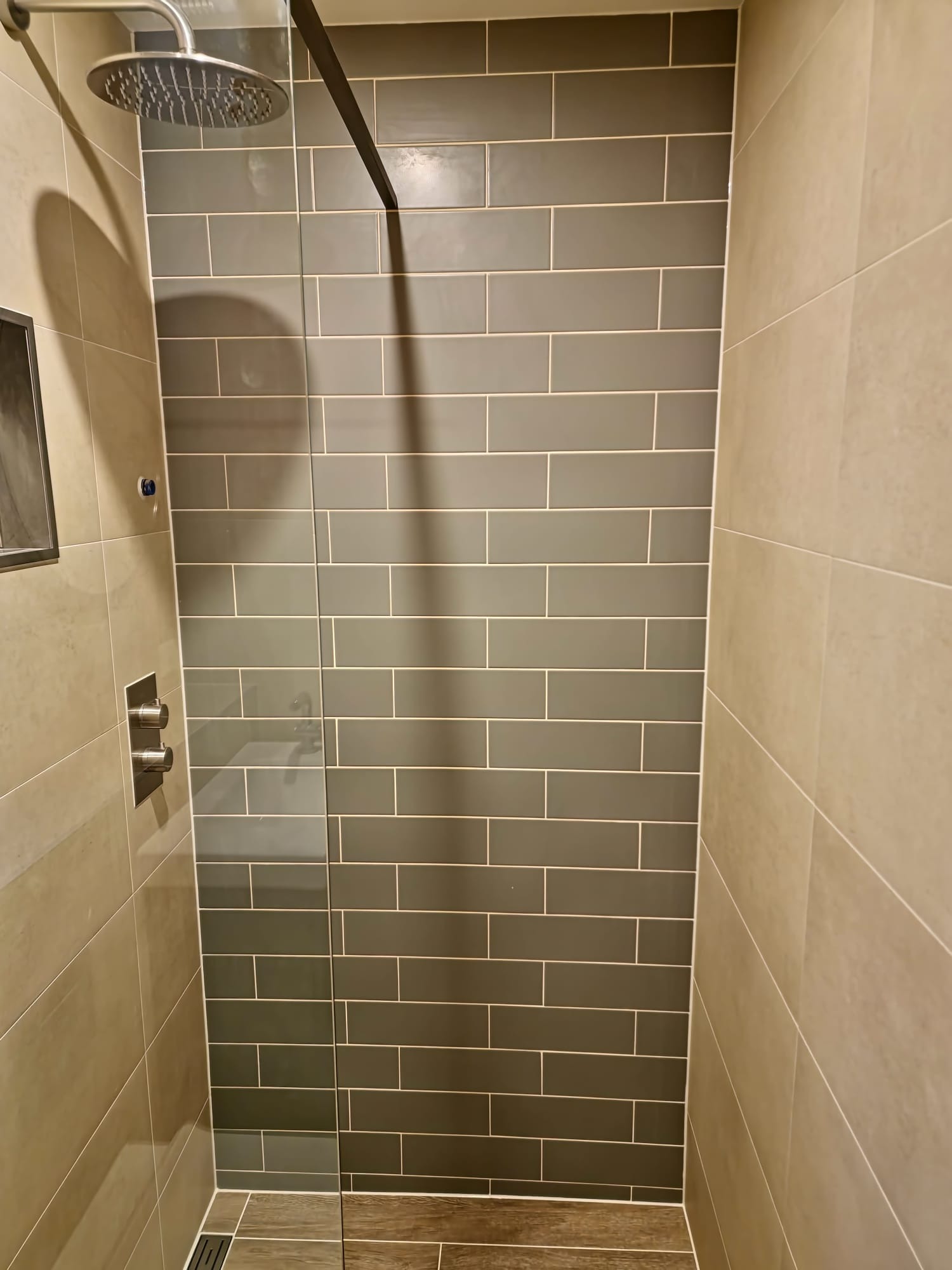 Nowoczesny prysznic z szarymi, prostokątnymi płytkami na ścianie, jasnymi płytkami po bokach, szklaną ścianką i deszczownicą.