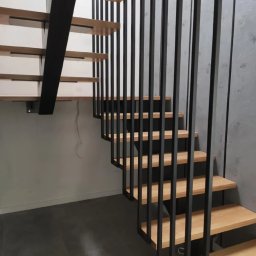 M&M BARTUZEL - Nowoczesne schody drewniane z czarną metalową konstrukcją nośną i pionowymi balustradami, widok z dołu, minimalistyczne wnętrze.