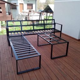 M&M BARTUZEL - Metalowy komplet mebli ogrodowych: ławka z oparciem, długa ławka bez oparcia i stolik kawowy, wykonane z czarnych profili, na drewnianym tarasie.