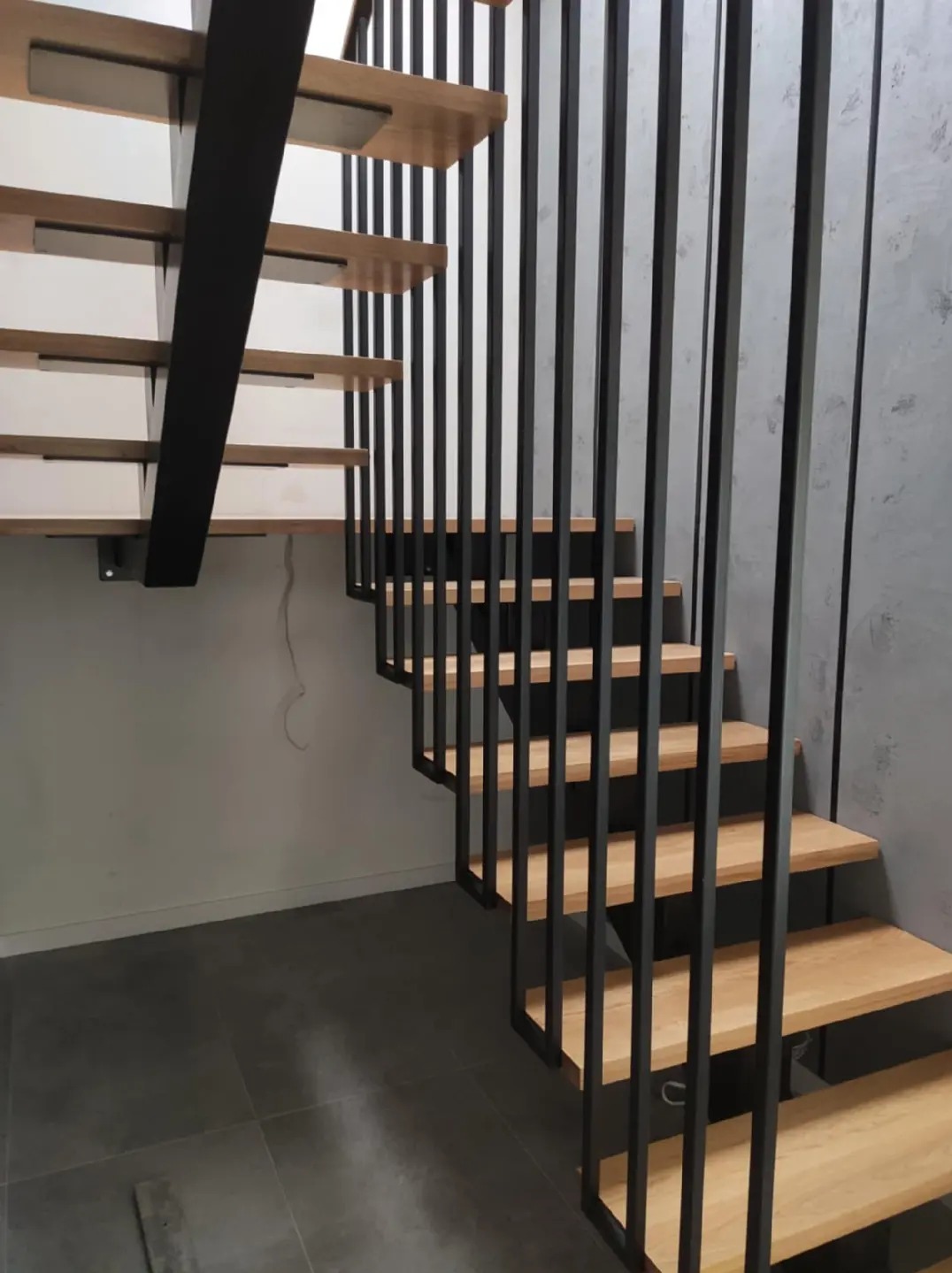 Nowoczesne schody drewniane z czarną metalową konstrukcją nośną i pionowymi balustradami, widok z dołu, minimalistyczne wnętrze.