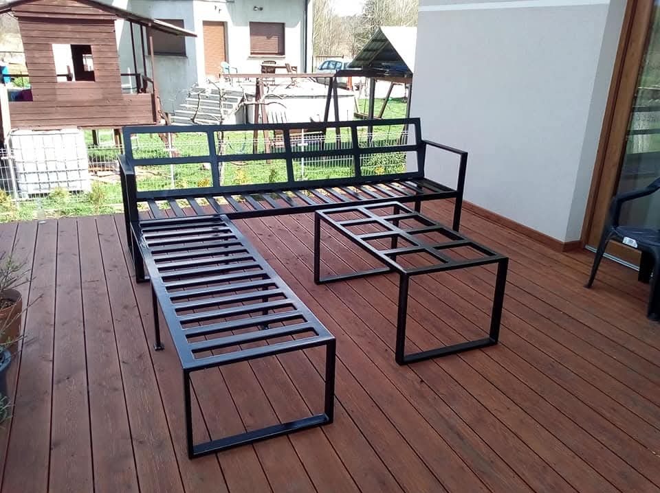 Metalowy komplet mebli ogrodowych: ławka z oparciem, długa ławka bez oparcia i stolik kawowy, wykonane z czarnych profili, na drewnianym tarasie.
