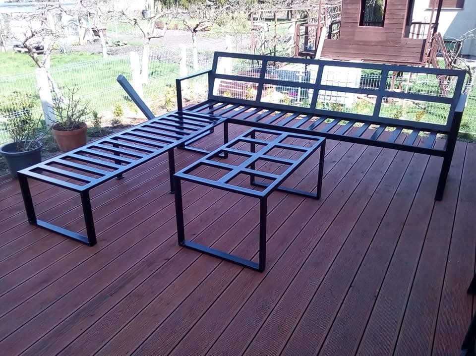 Czarny, metalowy komplet mebli ogrodowych: sofa, ławka i stolik kawowy, ustawione na drewnianym tarasie z widokiem na ogród.