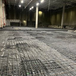 PÓŁNOC CHYCZEWSKA SPÓŁKA KOMANDYTOWA - Siatka zbrojeniowa ułożona na czarnej folii wewnątrz hali, przygotowana do zalania betonem pod fundamenty.