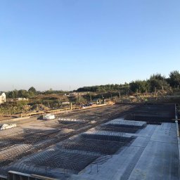 PÓŁNOC CHYCZEWSKA SPÓŁKA KOMANDYTOWA - Przygotowanie zbrojenia i wylewki betonowej pod fundamenty budynku, widoczne szalunki i pracownicy w oddali.