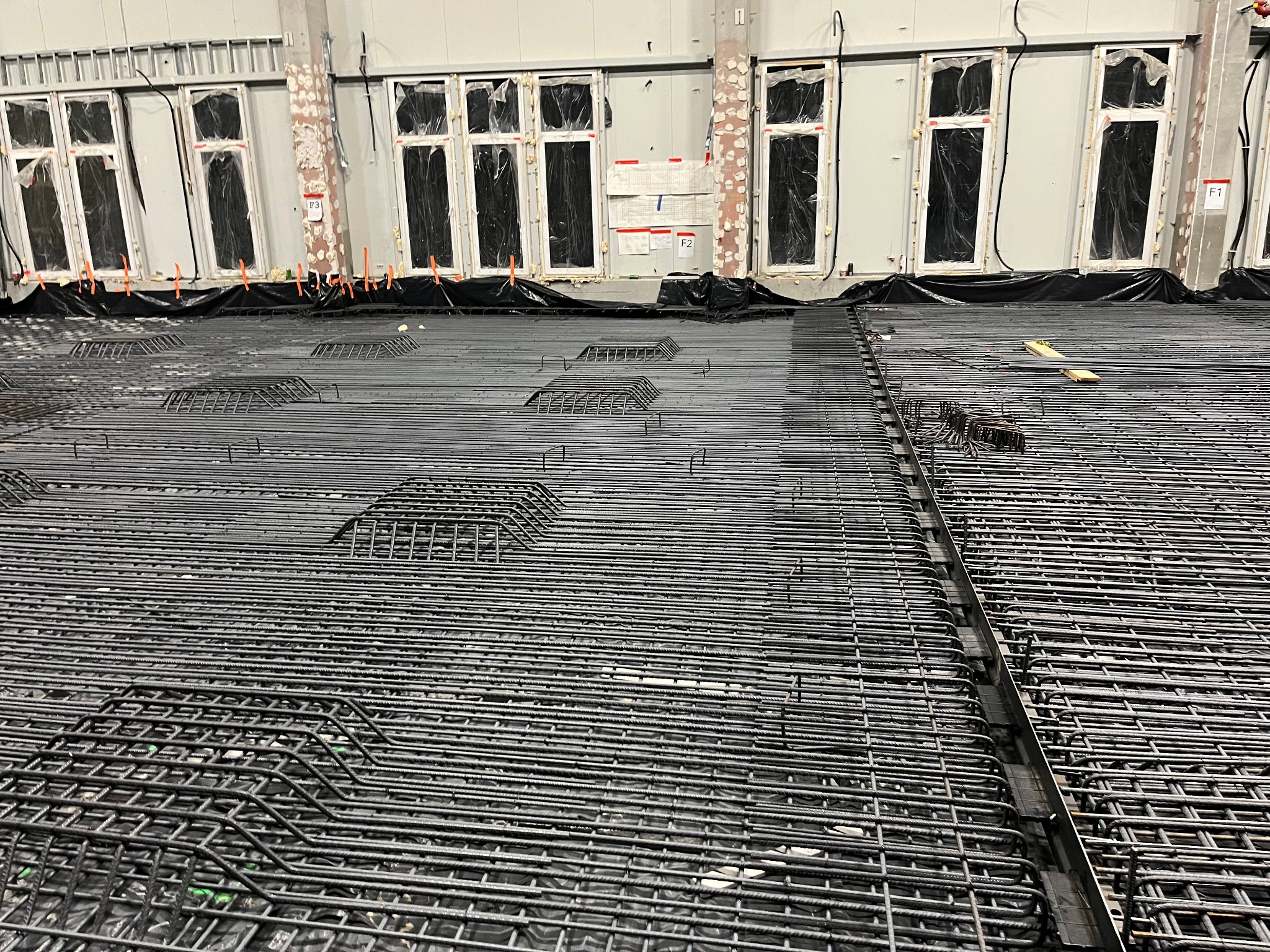 Zbrojenie ułożone na folii izolacyjnej, przygotowane do wylania fundamentów pod budynek z oknami zabezpieczonymi folią.