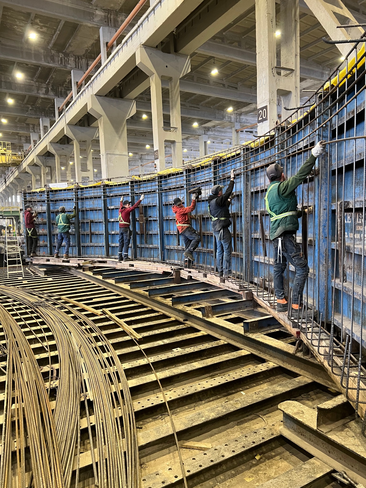 Pracownicy montują zbrojenie wewnątrz szalunku o okrągłym kształcie na budowie konstrukcji żelbetowej w hali przemysłowej