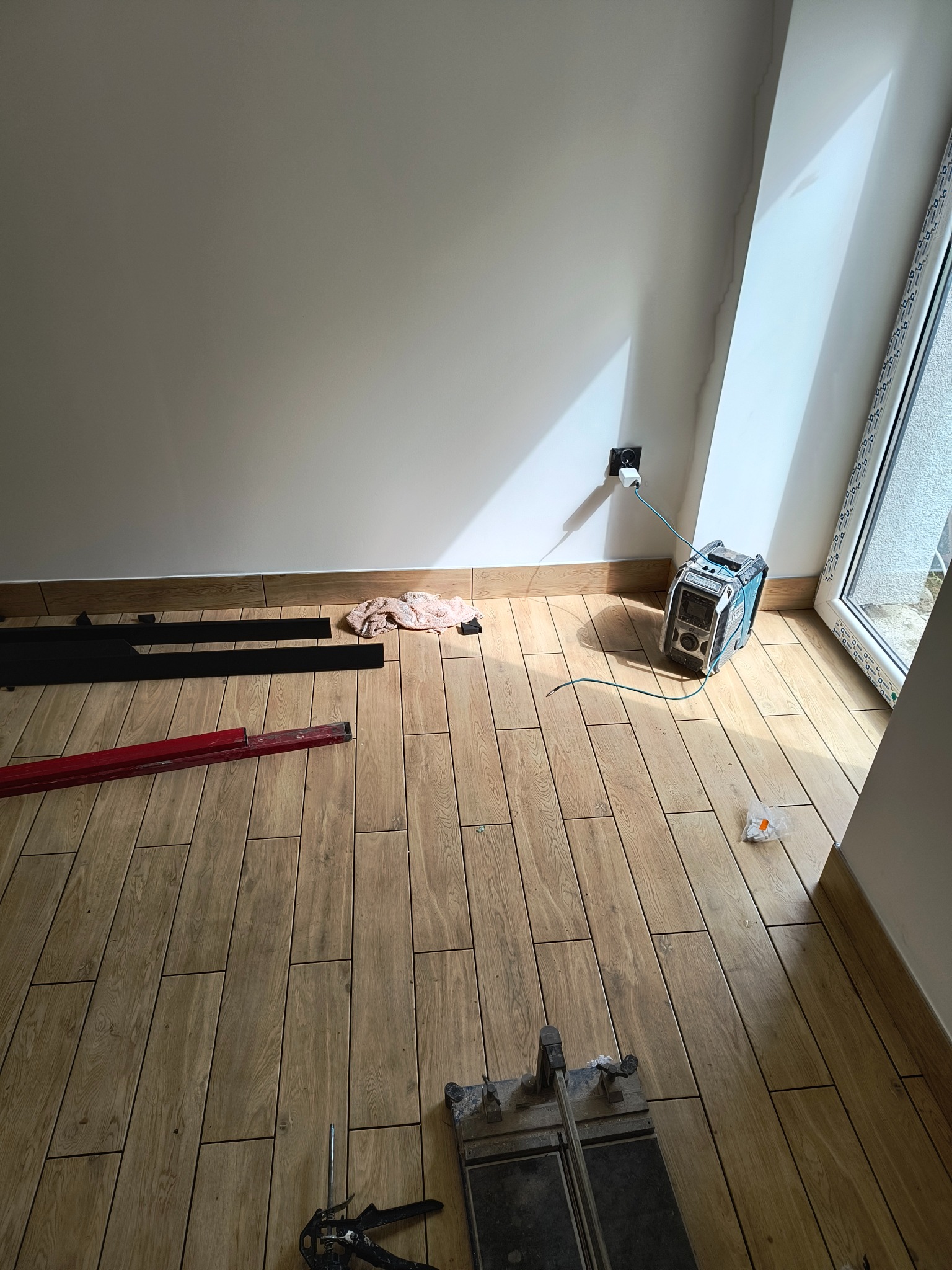 Ułożone panele podłogowe imitujące drewno w jasnym pomieszczeniu z widocznymi narzędziami: poziomica, listwy przypodłogowe i przecinarka do paneli, przy ścianie agregat prądotwórczy podłączony...