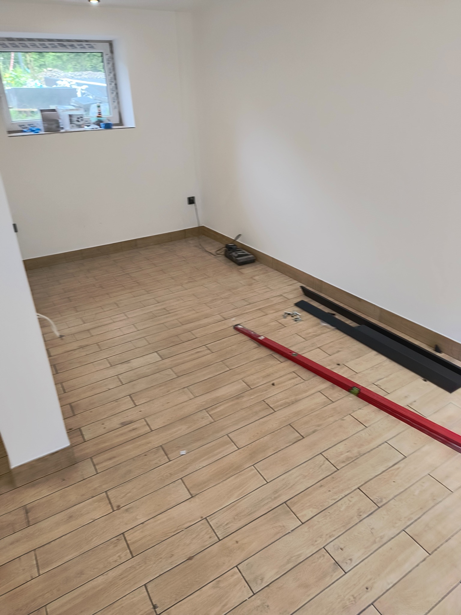 Pokój w trakcie układania paneli podłogowych: widoczny poziomica, listwy przypodłogowe i narzędzia.