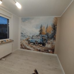 Mark-Art-Rem Marek Piwoński - Pokój po malowaniu z fototapetą przedstawiającą terenowy samochód na tle górskiego krajobrazu. Na podłodze leżą narzędzia i szczotka.