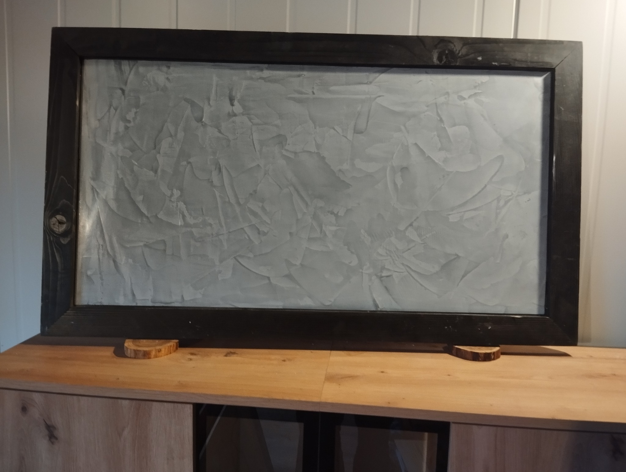 Dekoracyjna ściana z efektem stiuku w ramie, wykonana w Łaziskach Górnych. Unikalna faktura i ciemna rama dodają elegancji wnętrzu. Wykończenie na drewnianej komodzie.