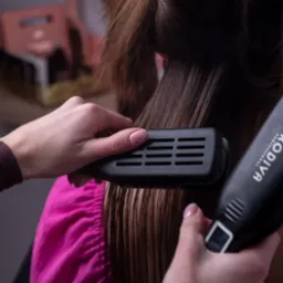 Prostowanie wilgotnych włosów prostownicą marki Prodiva, widoczne dłonie stylistki z delikatnym manicure.