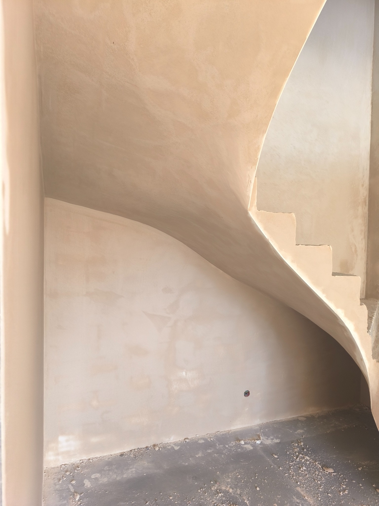 Wnętrze w trakcie prac wykończeniowych: ściany i schody pokryte świeżo nałożoną, jasną gładzią. Widoczny fragment instalacji elektrycznej. Surowe wykończenie podłogi.