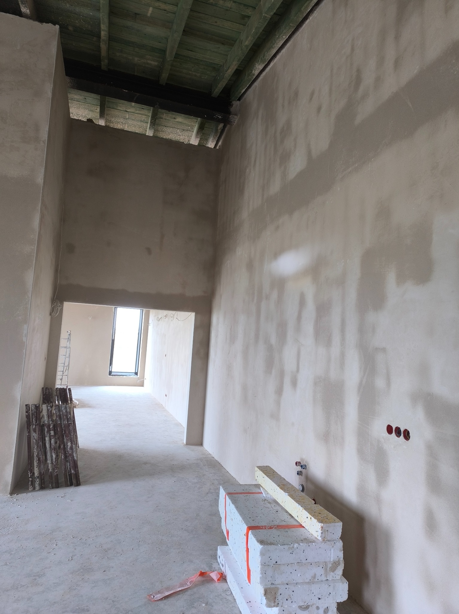 Wnętrze w trakcie szpachlowania: surowe ściany, widoczne puszki elektryczne, materiały budowlane. Ujęcie z dołu, wysokie pomieszczenie z drewnianym stropem.