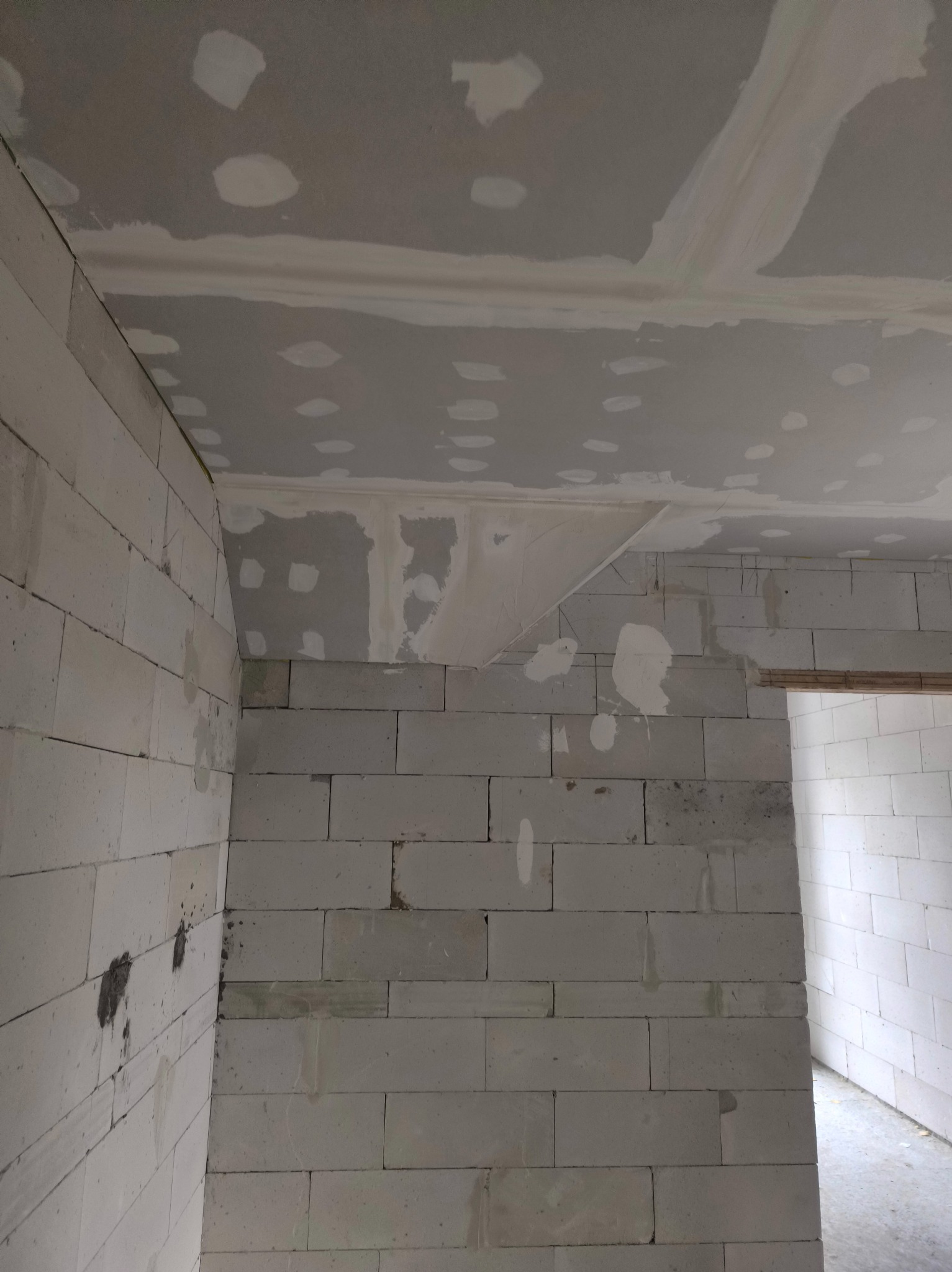 Surowy stan wnętrza z bloków, częściowo pokrytego szpachlą na suficie i ścianach. Widoczne niedoskonałości i przygotowanie do dalszych prac wykończeniowych.