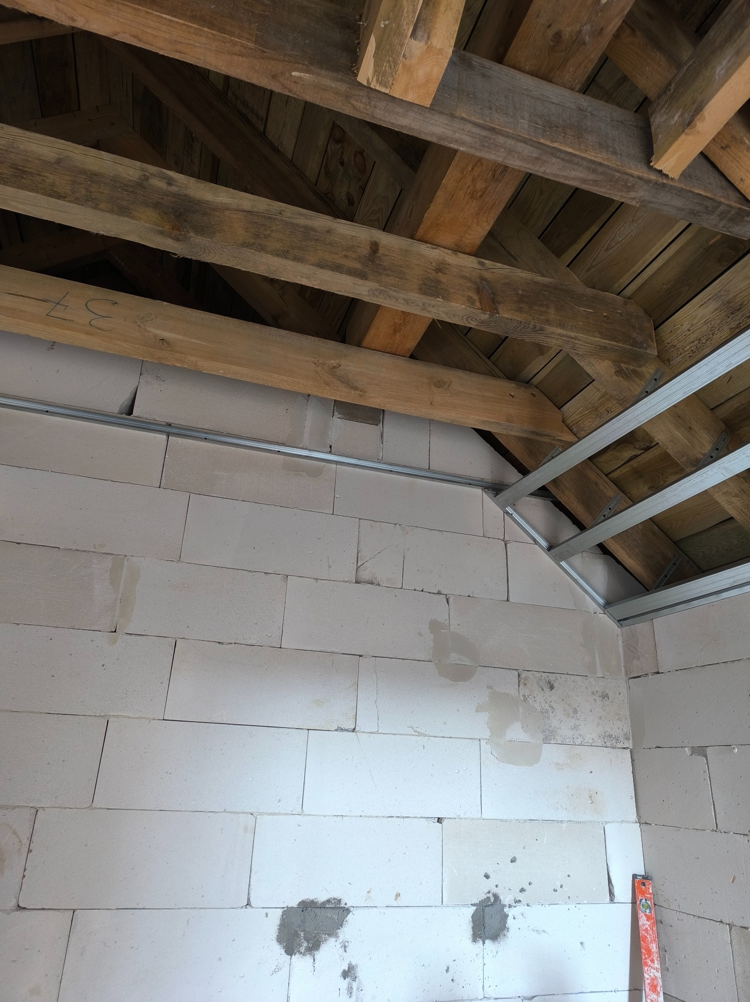 Wnętrze w trakcie prac wykończeniowych: ściany z betonu komórkowego, drewniana więźba dachowa i metalowa konstrukcja sufitu podwieszanego.