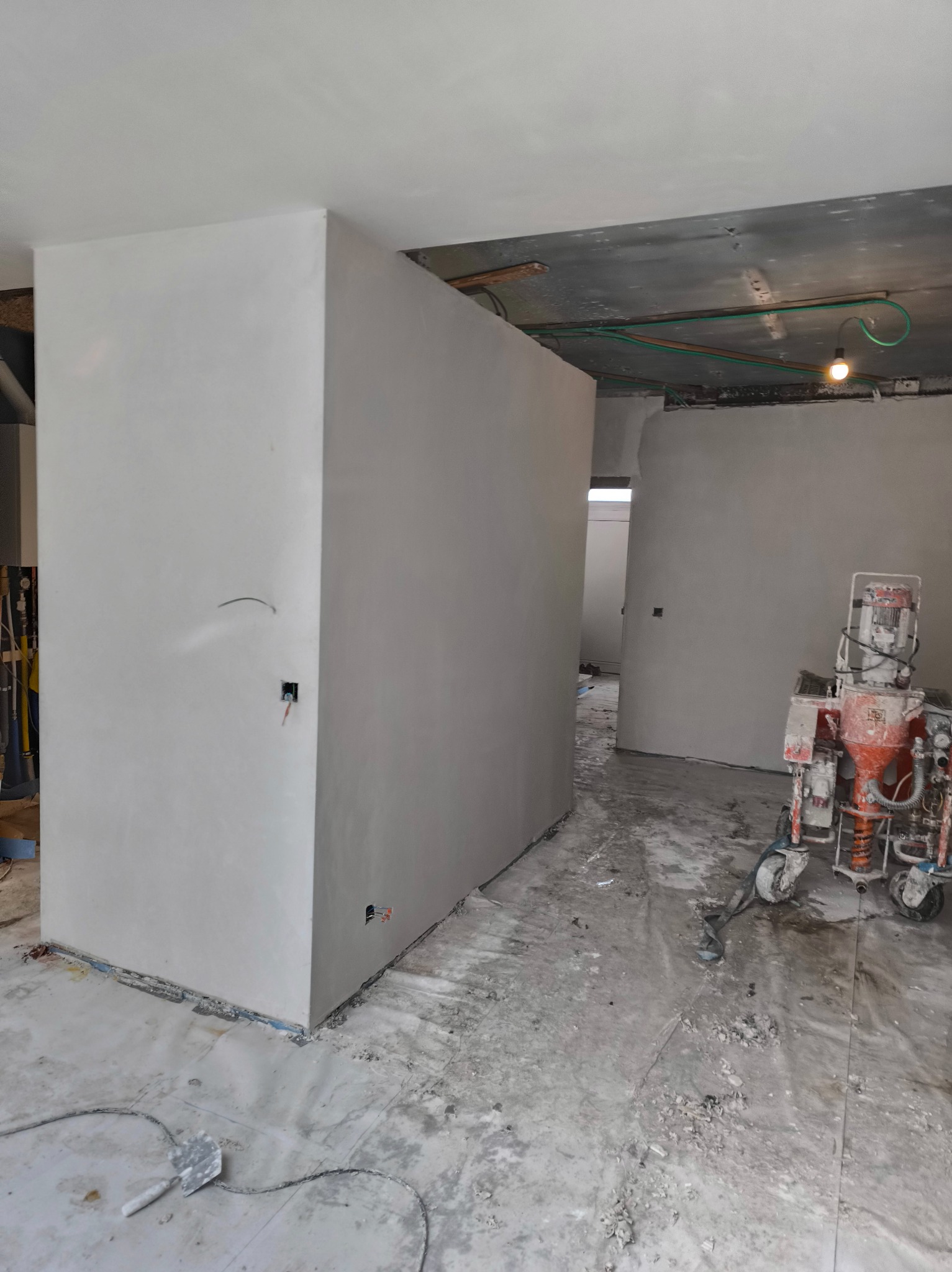 Wnętrze w trakcie prac wykończeniowych: gładkie, jasne ściany po szpachlowaniu, widoczny agregat malarski i narzędzia, surowy sufit.