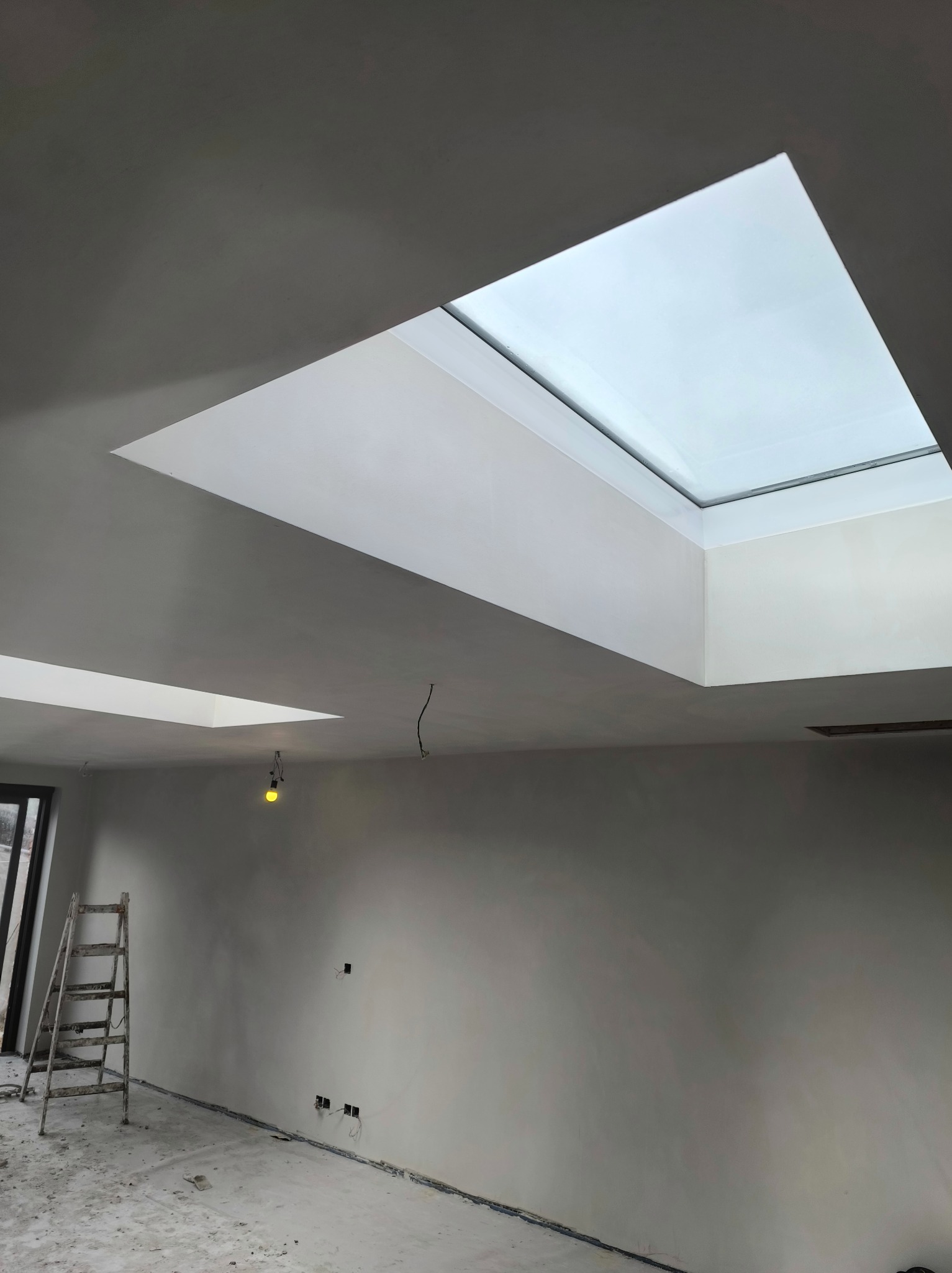 Wnętrze po szpachlowaniu z oknami dachowymi. Widoczna drabina, surowe ściany i podłoga. Przygotowanie do dalszych prac wykończeniowych.