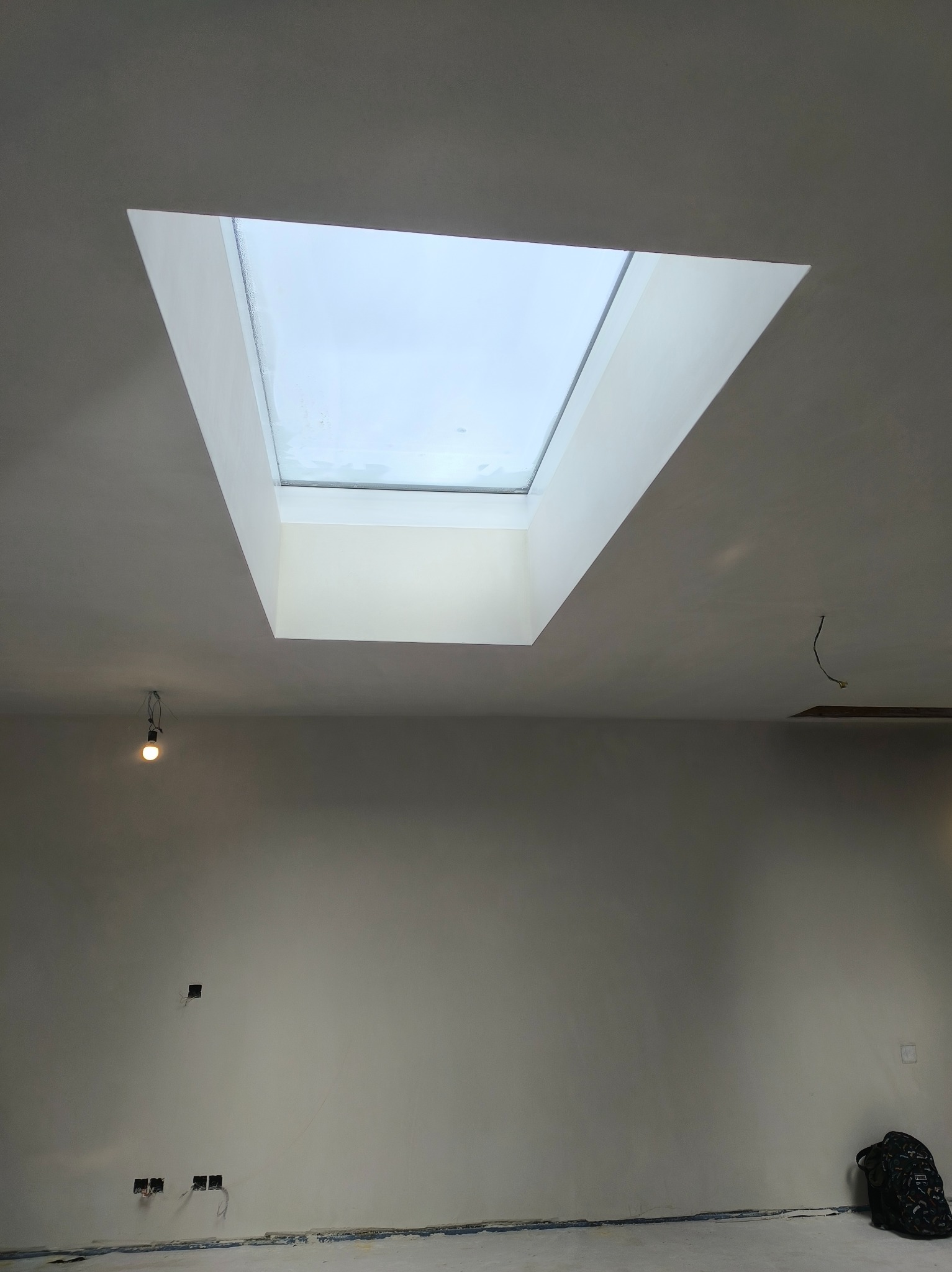 Wnętrze pokoju po szpachlowaniu, widoczne gładkie ściany i sufit z oknem dachowym. Na podłodze widoczne ślady po pracach wykończeniowych.