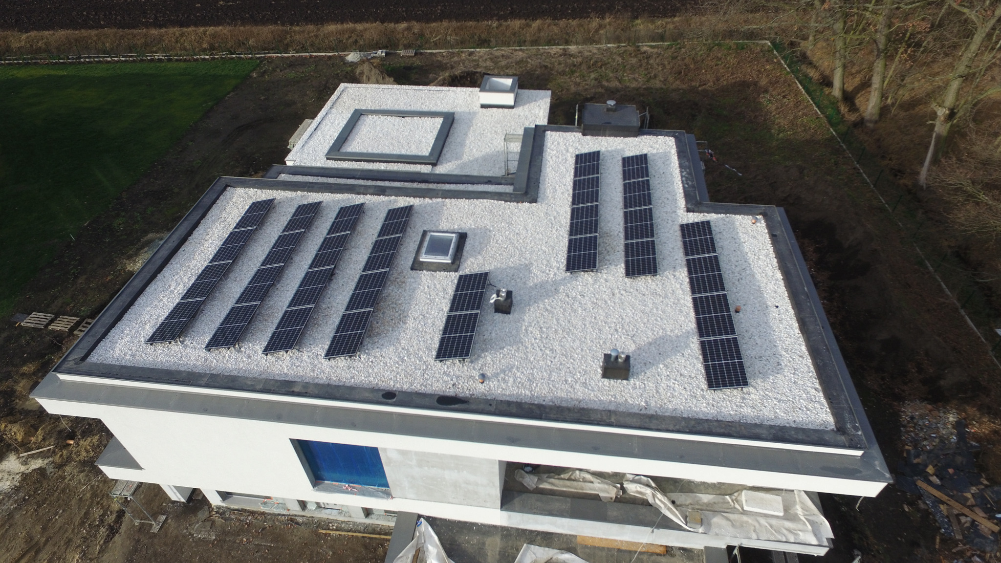Nowoczesny, płaski dach pokryty białym żwirem z zamontowanymi panelami fotowoltaicznymi, widok z góry na dom w trakcie budowy.