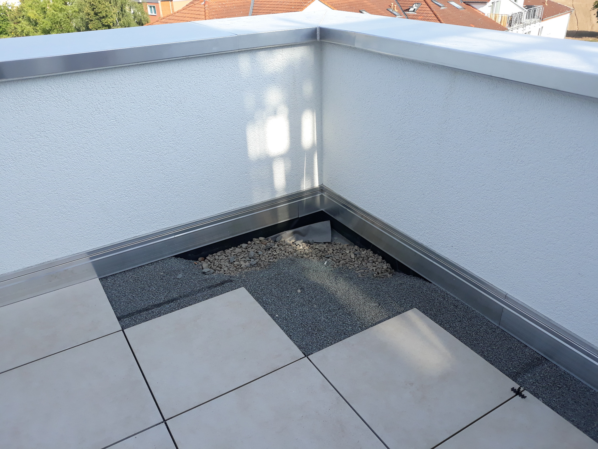 Wykończony narożnik balkonu z szarymi płytkami, obróbką blacharską i drenażem z kamyków, widok z góry.