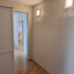 BART ART WYKOŃCZENIA Bartłomiej Jarosz - Jasne, świeżo pomalowane ściany w korytarzu z parkietem w Legnicy. Widoczne dwa kwadratowe kinkiety i drzwi w głębi. Minimalistyczny design.