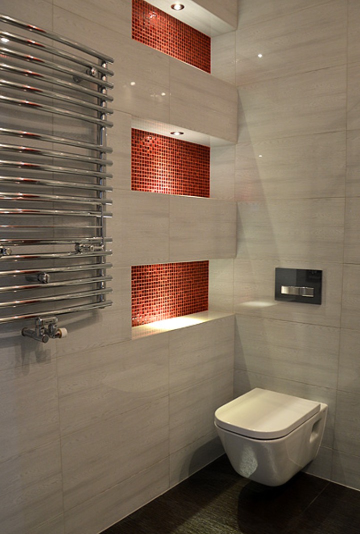 Nowoczesna łazienka z podwieszaną toaletą, grzejnikiem drabinkowym i wnękami z czerwoną mozaiką, oświetlona punktowo.
