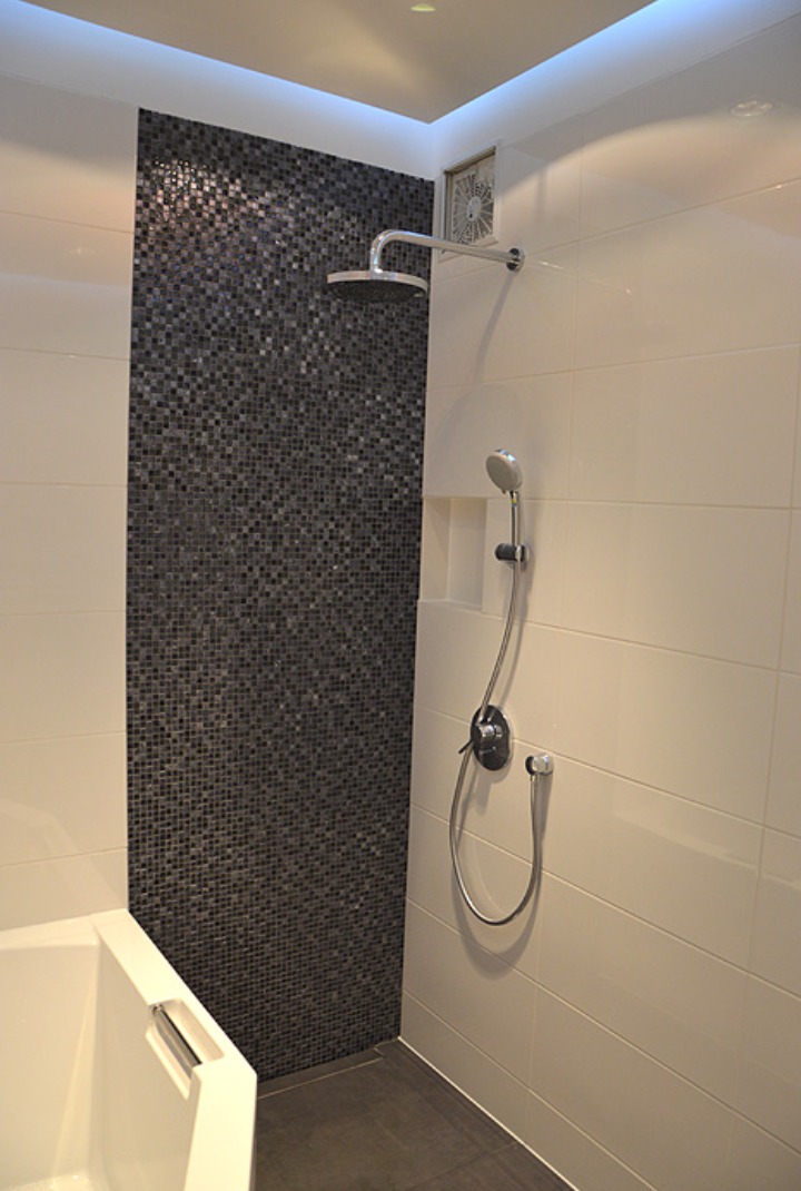 Nowoczesna łazienka z białymi płytkami, akcentem z mozaiki grafitowej pod prysznicem, baterią termostatyczną i oświetleniem LED podsufitowym.