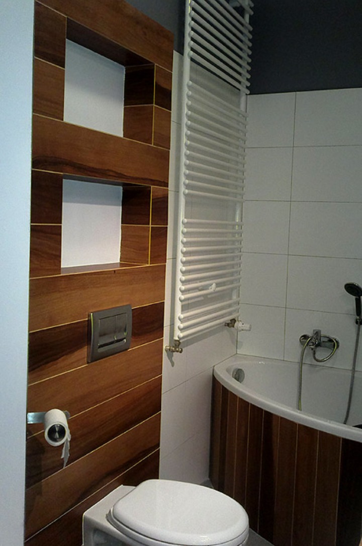 Nowoczesna łazienka z drewnianą zabudową ściany z wnękami, grzejnikiem drabinkowym i obudową wanny z tego samego materiału.