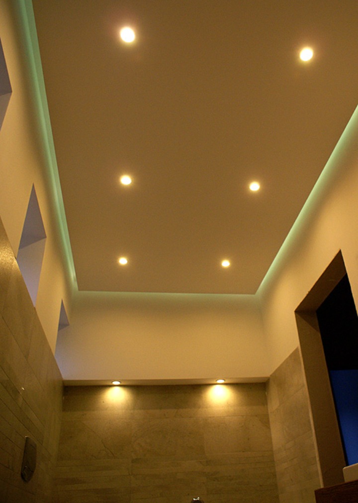 Nowoczesna łazienka z podwieszanym sufitem, oświetleniem LED i płytkami imitującymi kamień na ścianach.