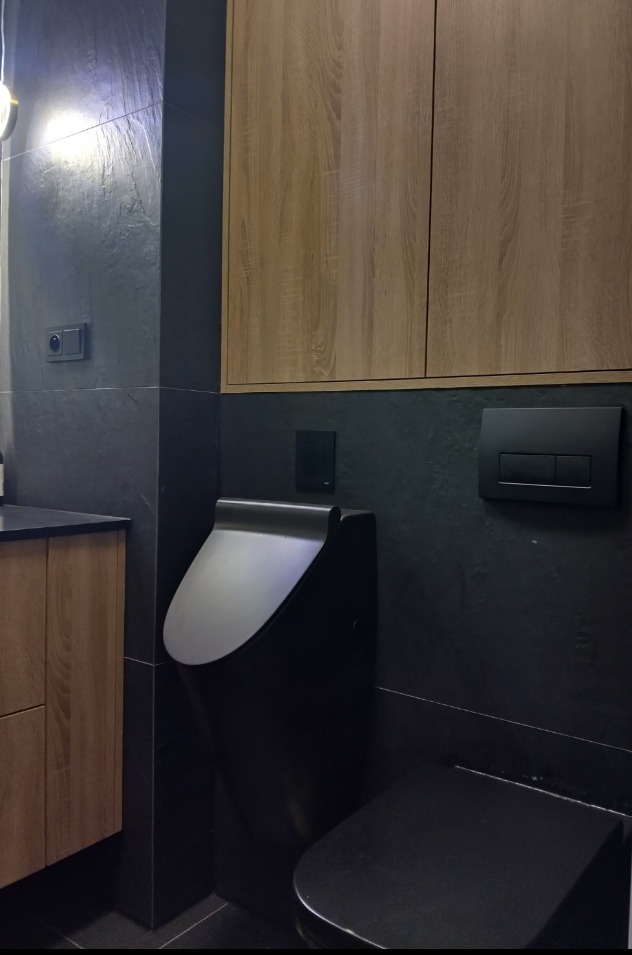 Nowoczesna łazienka z wiszącą toaletą w kolorze czarnym, drewniane szafki i czarne płytki na ścianach, minimalistyczny design.