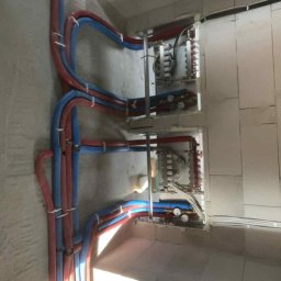 Hydro-Therm Mikołaj Janca - Rozdzielacze ogrzewania podłogowego z rurami PEX (czerwone i niebieskie) zamontowane na surowej ścianie w nowym budownictwie. Widok z góry.