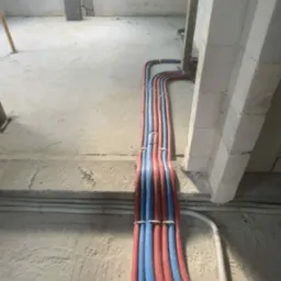 Ściana z instalacją rurową w kolorach czerwonym i niebieskim, przytwierdzoną do ściany w surowym stanie, z widocznym oknem dachowym w tle.