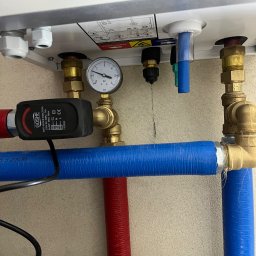 Hydro-Therm Mikołaj Janca - Szczegółowe ujęcie instalacji CO z manometrem, zaworami i rurami w kolorze niebieskim i czerwonym. Widoczne elementy kotła i czujnik GOSHE.