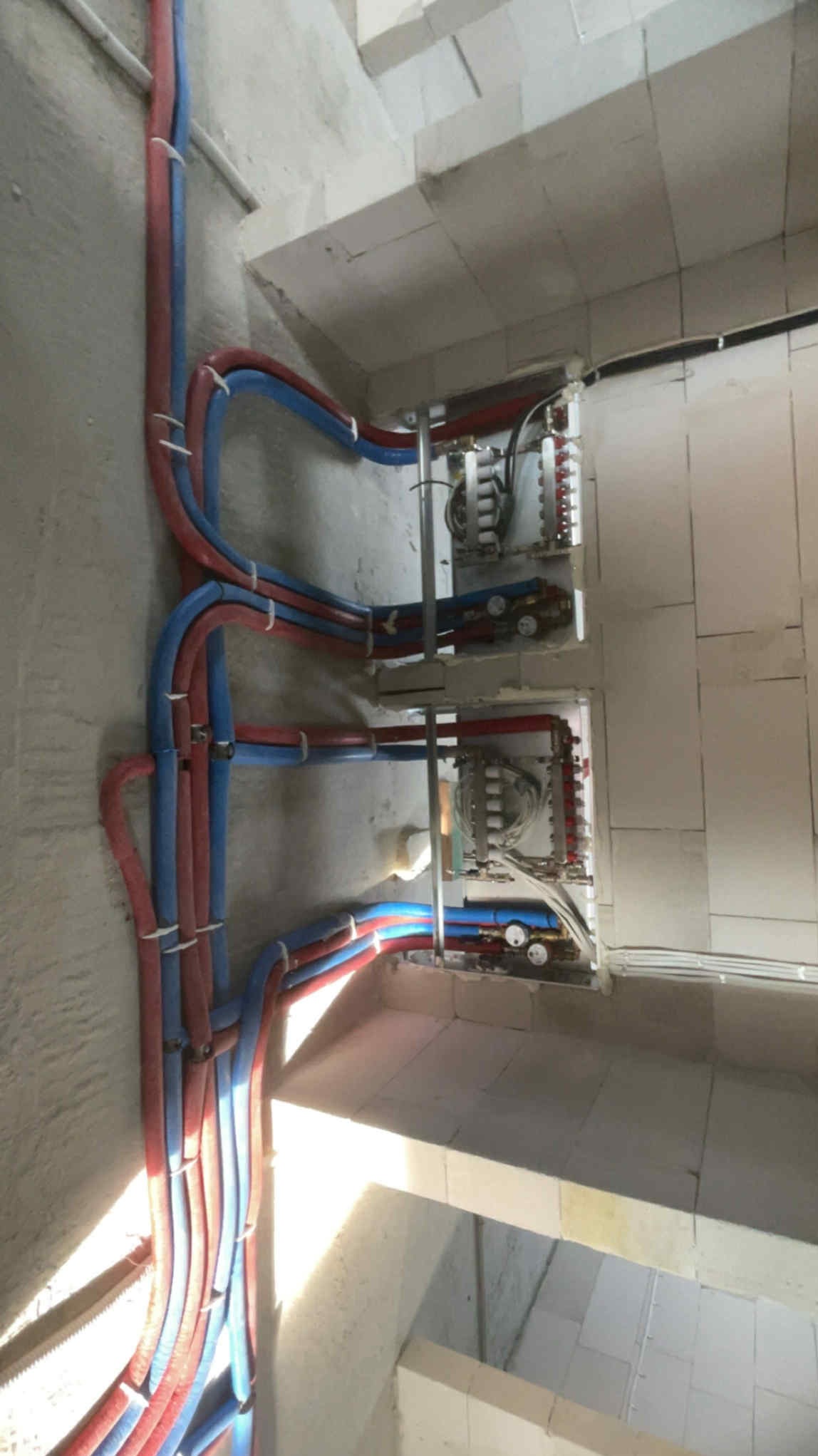 Rozdzielacze ogrzewania podłogowego z rurami PEX (czerwone i niebieskie) zamontowane na surowej ścianie w nowym budownictwie. Widok z góry.