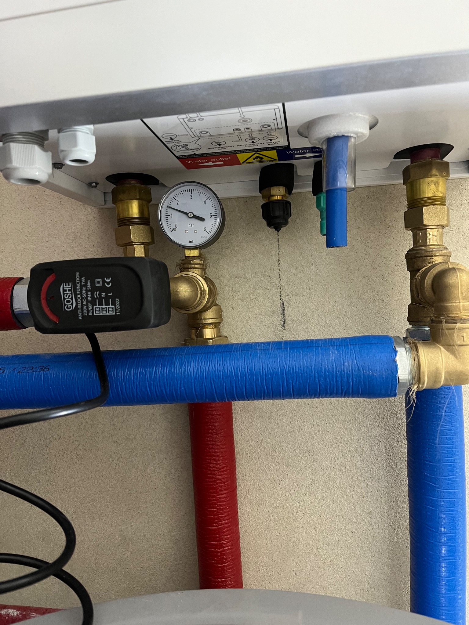 Szczegółowe ujęcie instalacji CO z manometrem, zaworami i rurami w kolorze niebieskim i czerwonym. Widoczne elementy kotła i czujnik GOSHE.