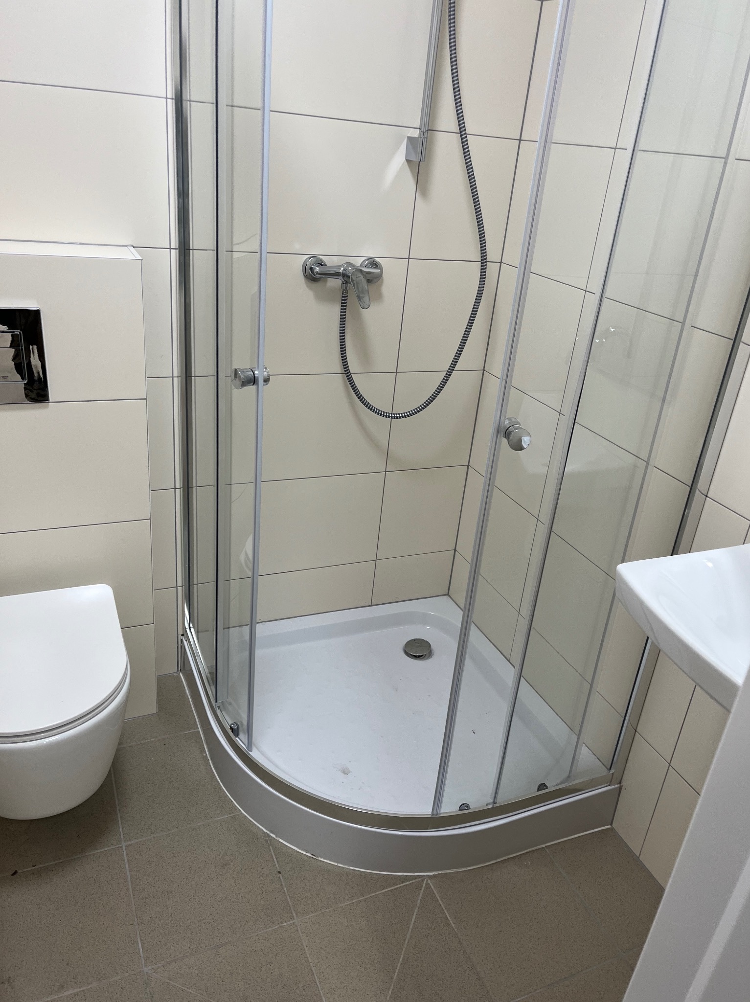 Nowoczesna kabina prysznicowa narożna z chromowaną armaturą, umywalką i toaletą w jasnej łazience z beżowymi płytkami. Widok z góry.