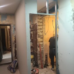 Firma budowlano-wykonczeniowa Gregor Grzegorz Małachowski - Montaż ścianki działowej z płyt gipsowo-kartonowych w trakcie remontu, widoczne profile metalowe, fragment starej ściany z cegły, narzędzia i materiały budowlane.