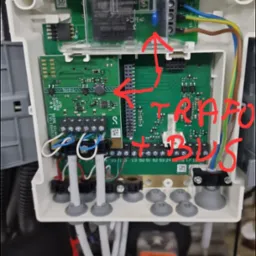 Otwarta obudowa sterownika z widocznymi płytkami drukowanymi, transformatorem i złączami kablowymi, oznaczona czerwonymi napisami 'TRAFO + BUS'.