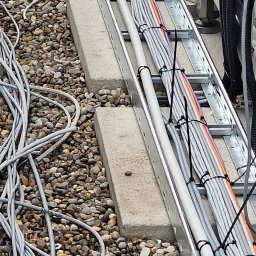 WOMAX Wojciech Wojs - Uporządkowane kable elektryczne prowadzone po metalowej drabince, zabezpieczone czarnymi opaskami, na tle żwirowego dachu.