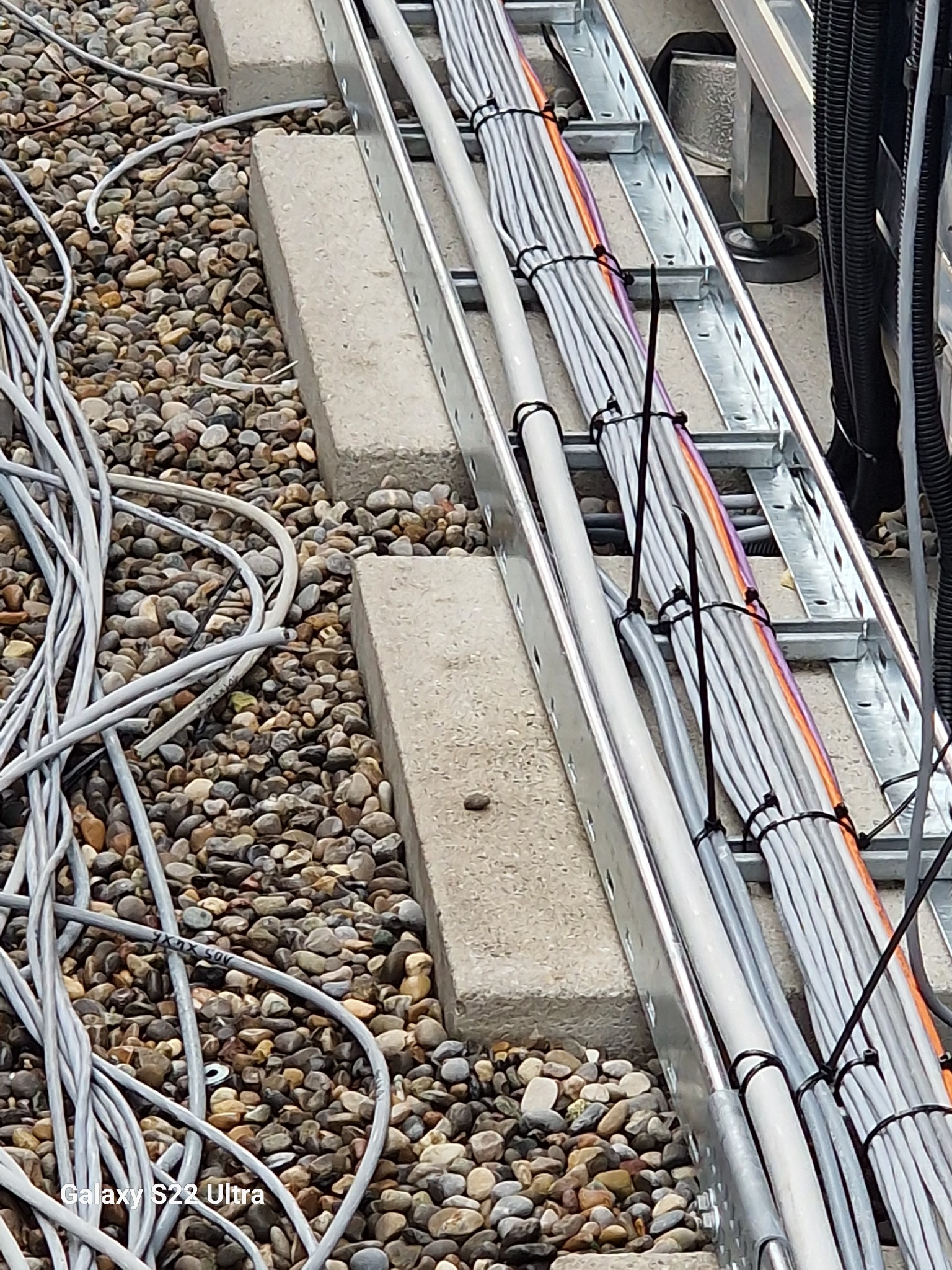 Uporządkowane kable elektryczne prowadzone po metalowej drabince, zabezpieczone czarnymi opaskami, na tle żwirowego dachu.