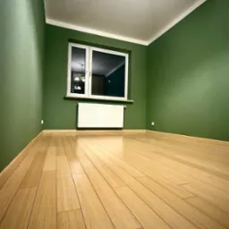 Pusty pokój po remoncie: ściany pomalowane na oliwkowy kolor, jasna drewniana podłoga, biały grzejnik pod oknem, widoczne listwy przypodłogowe.