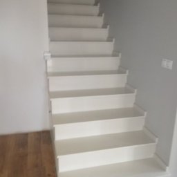 Komi - Nowoczesne, białe schody z drewnianą podłogą i szarą ścianą, widoczne z dołu, z delikatnym oświetleniem.