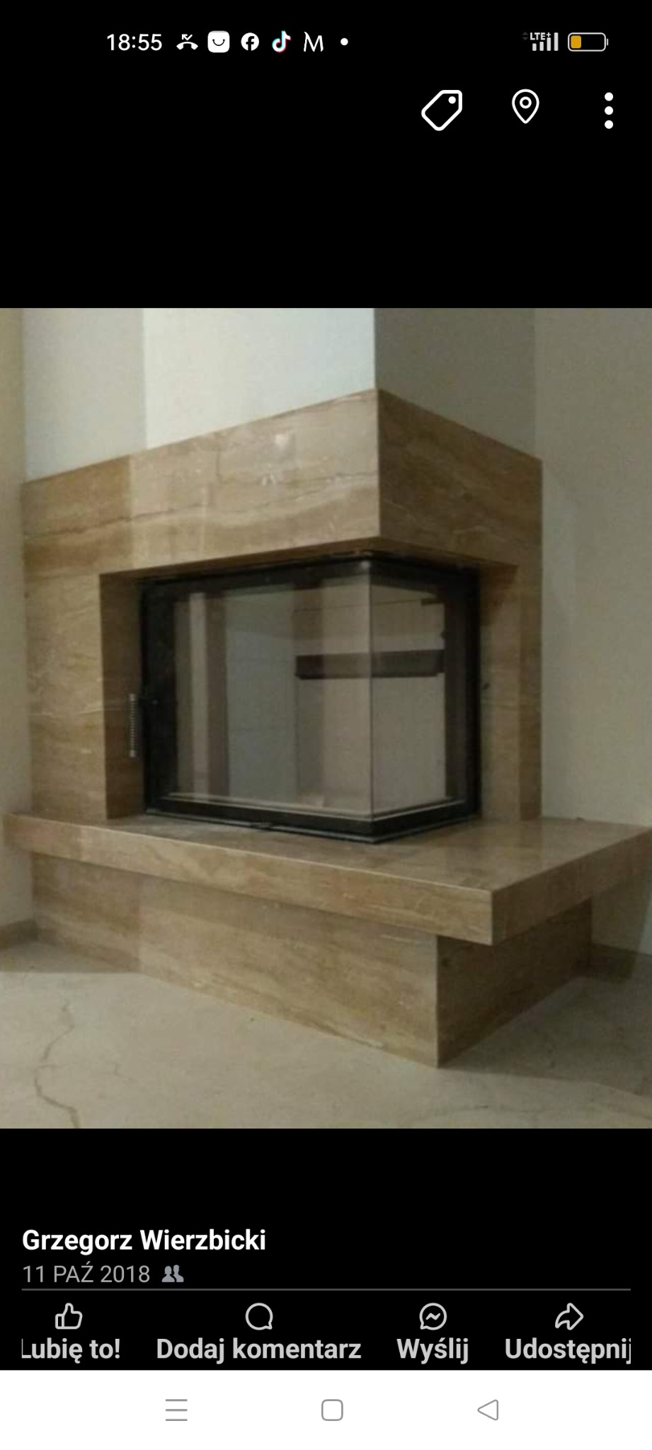 Obudowa kominkowa z jasnego trawertynu z przeszklonym wkładem kominkowym o czarnych ramach.