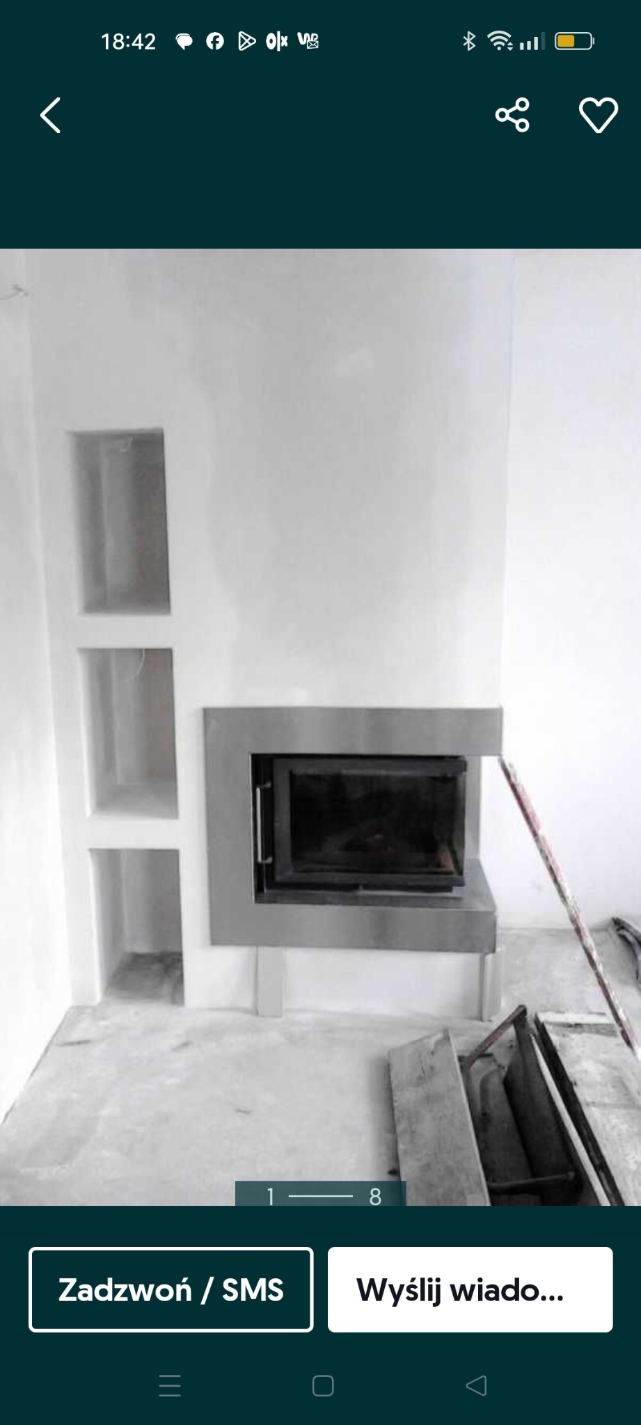 Wnęki ścienne obok kominka z metalowym obramowaniem i szarą, surową podłogą w trakcie prac wykończeniowych.