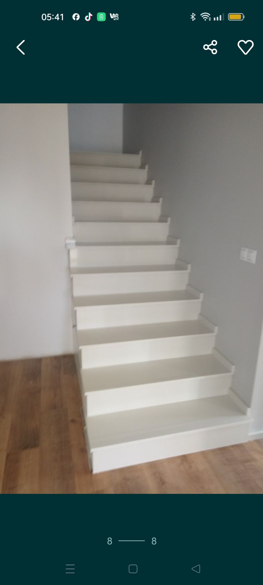 Nowoczesne, białe schody z drewnianą podłogą i szarą ścianą, widoczne z dołu, z delikatnym oświetleniem.