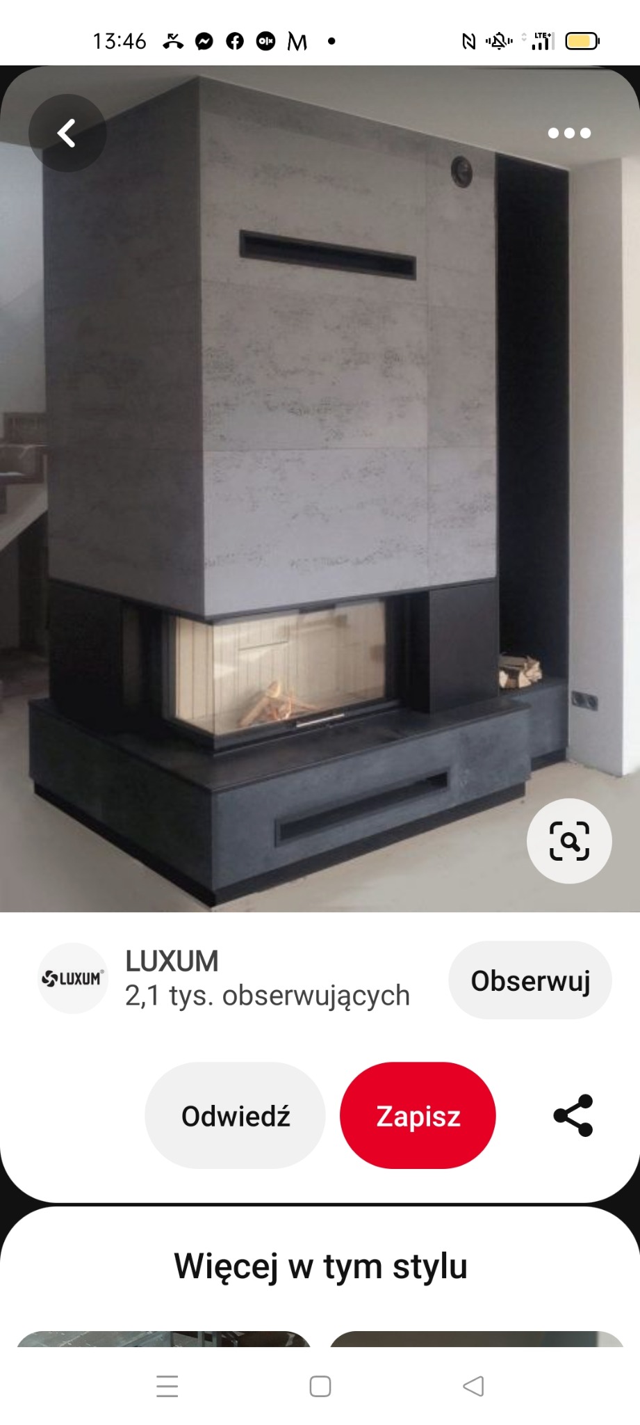 Nowoczesny kominek narożny z obudową z szarego betonu architektonicznego i czarnymi akcentami, z widocznym drewnem w palenisku i ułożonymi szczapami obok.