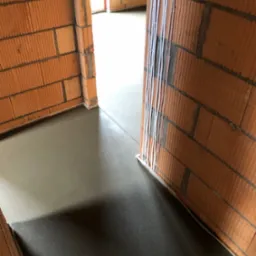 Świeżo wylana, gładka posadzka w surowym wnętrzu z ceglanymi ścianami i pionowymi rurami wzdłuż framugi drzwi.