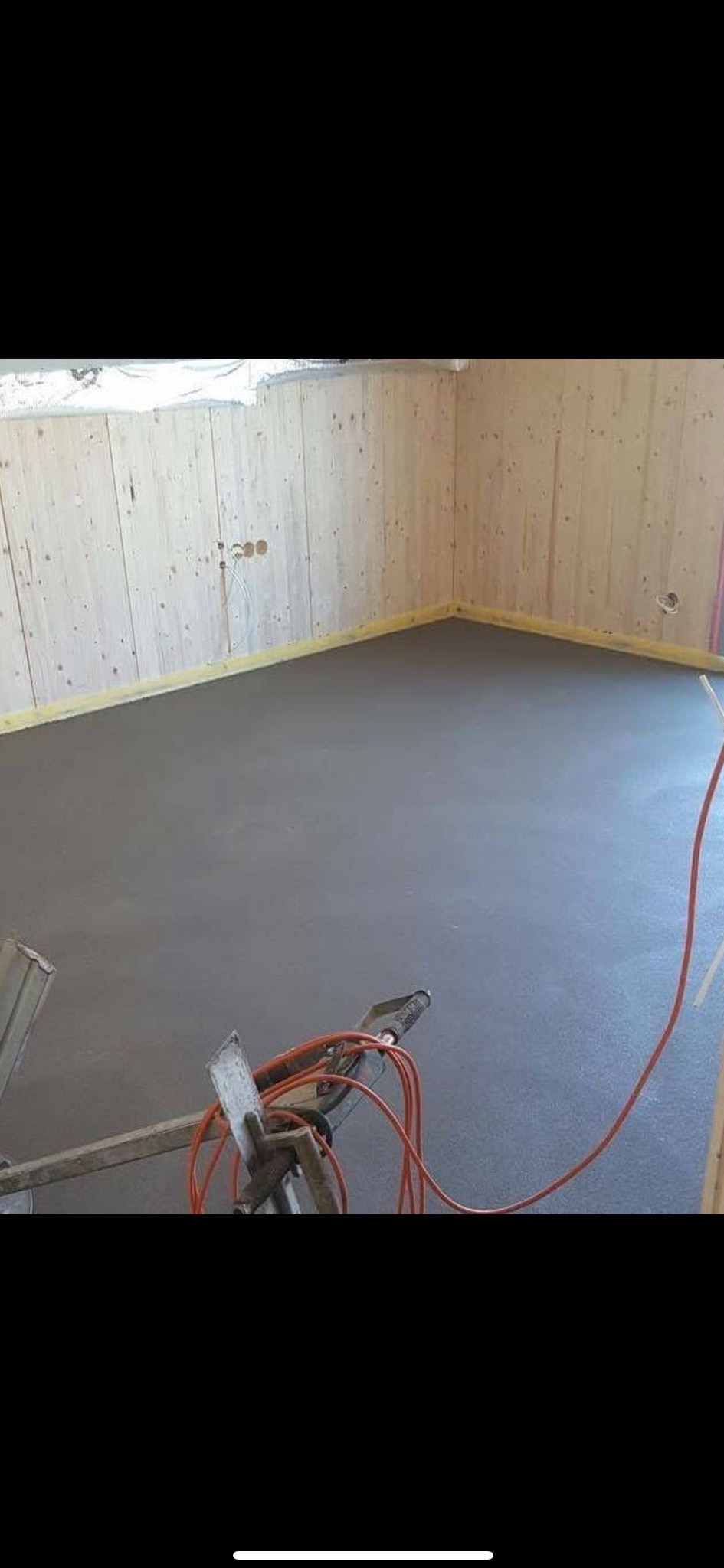 Świeżo wylana, gładka, szara posadzka w pomieszczeniu z boazerią, widoczne narzędzia i kable.