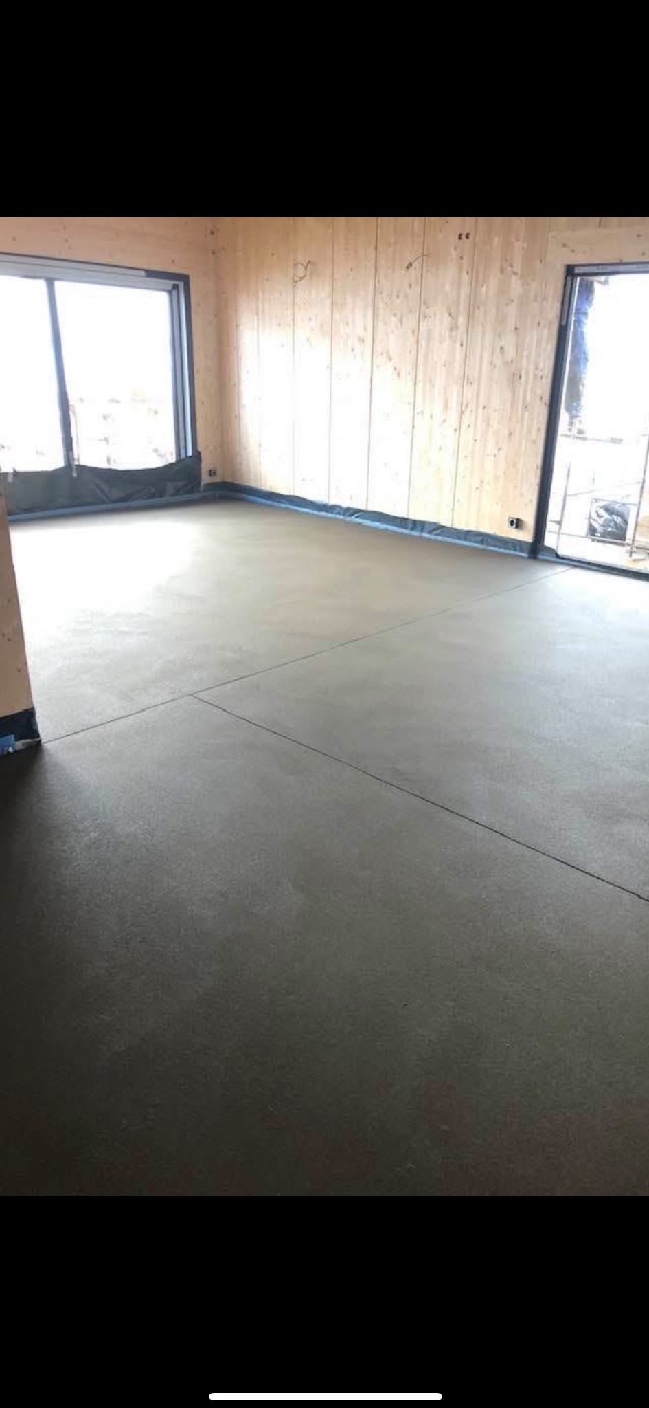 Wylana, gładka posadzka w surowym wnętrzu z drewnianymi ścianami i dużymi oknami, zabezpieczonymi folią malarską.