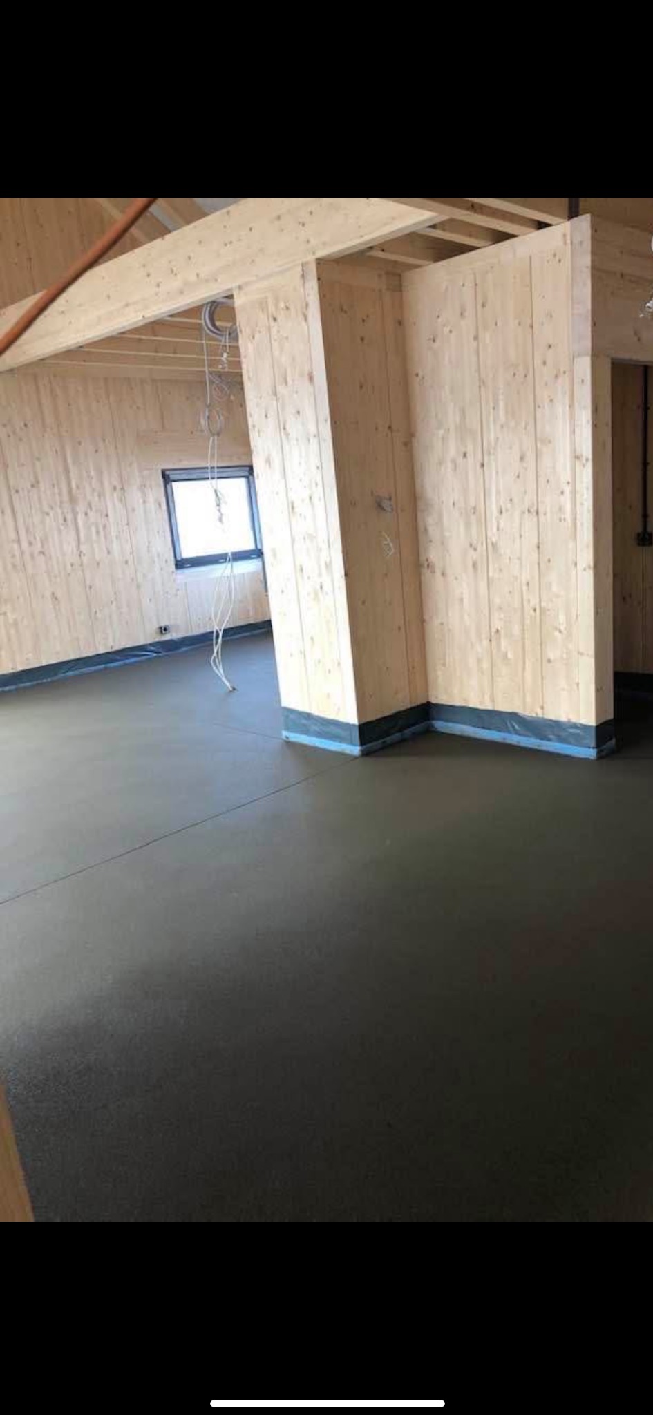 Wnętrze budynku w surowym stanie z wylaną, gładką, ciemną posadzką i drewnianymi ścianami oraz elementami konstrukcyjnymi.